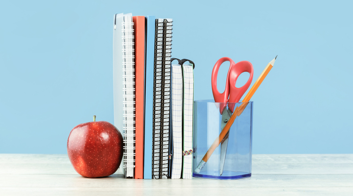 Organized office and school orange and pastel blue stationery, notebooks pencils scissors and alarm clock with red apple on grey wooden desk. Copy space for back to school education and craft concept