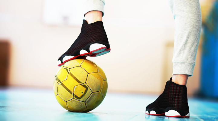 Två fötter varav den vänstra stödjer på en gul fotboll