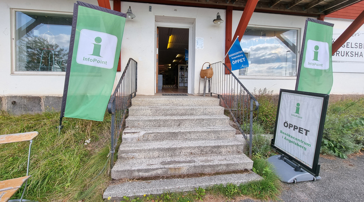 Entre till Besökscentrum/brukshandeln. Gröna beachflaggor på var sida av entrén. 7 trappsteg. 