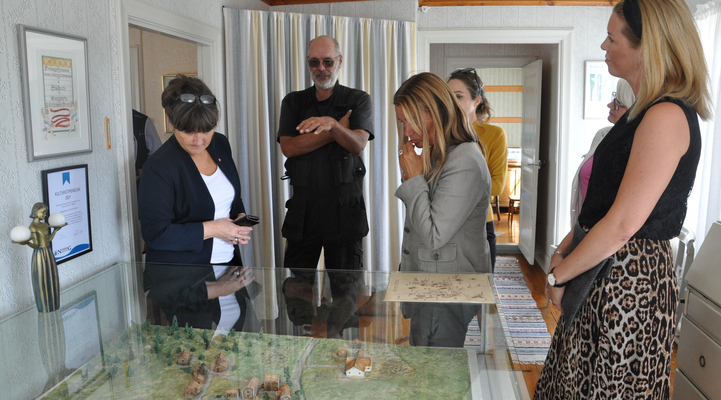 Några av deltagarna på ministerbesöket befinner sig inne i ett hus på Brategården och tittar på ett landskap som är byggt i miniatyr och står i en monter.