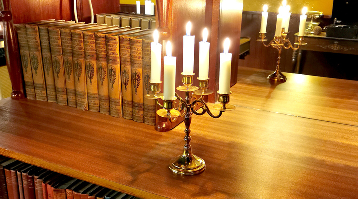 Interiörbild från Wärdshuset. Brinnande ljus i en kandelaber. Böcker i bakgrunden.