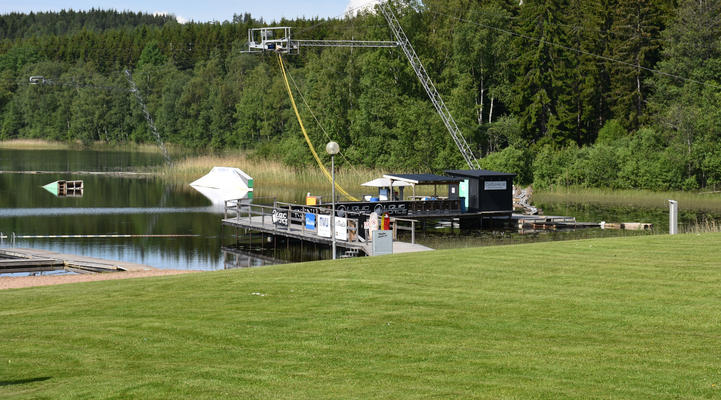 Grön gräsmatta, sjön och Cable Parken vid Eskiln