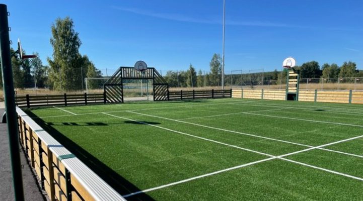 Näridrottsplatsen i Uggelbo. Grön konstgräsplan med staket runt om. Tre basketkorgar syns och planen är linjerad för olika sporter.