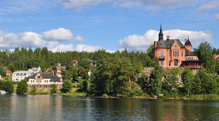 Till höger, Villa Ulvaklev. En byggnad med rött tegel och torn med spiror. Till vänster i bild, Ängelsbergs station. En gul byggnad med svart skiffertak.
