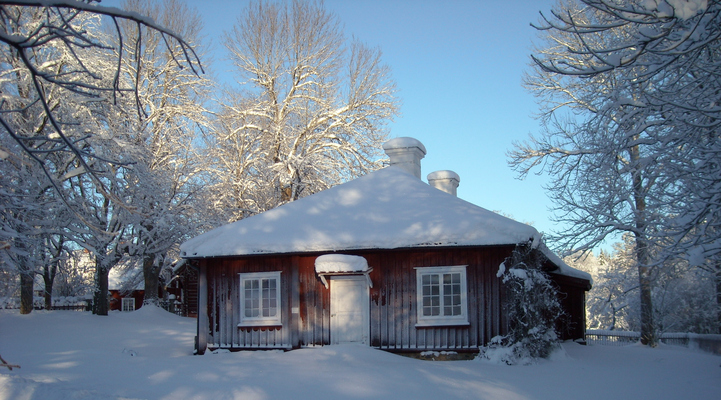 Byggnaden kallat "Krogen". Ett snötäckt rött trähus med vita fönster och dörrar. Snö på både mark och tak